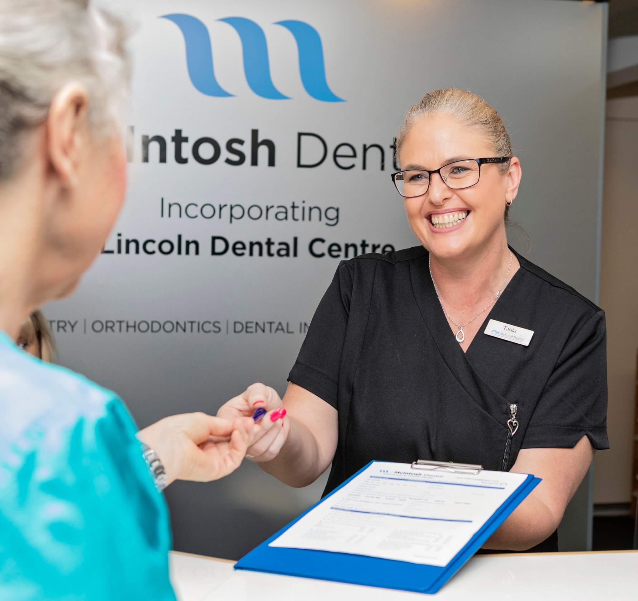McIntosh Dental vacancies, dental receptionist handing clipboard to patient